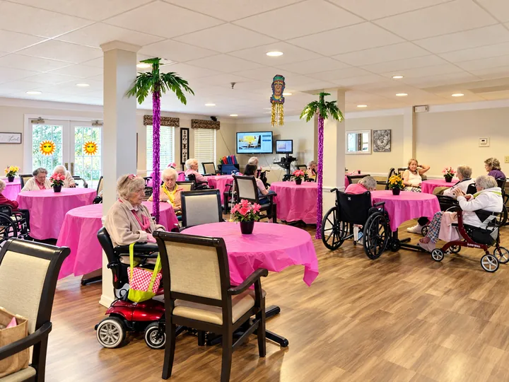 The Regency House dining room decorated with palm trees and pink tablecloths for a party, with residents seated at the tables