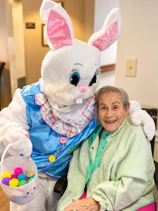 A resident smiling beside a visitor in an Easter Bunny costume holding a basket of eggs