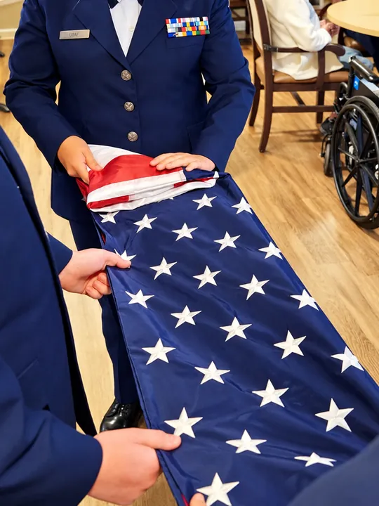 Service members in dress uniform folding an American flag in the Regency House dining room