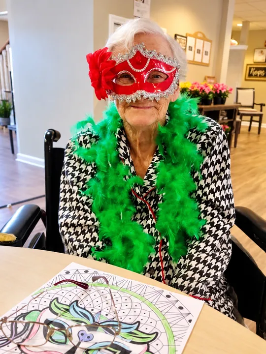 A resident in a red sequined mask and green feather boa with a coloring page