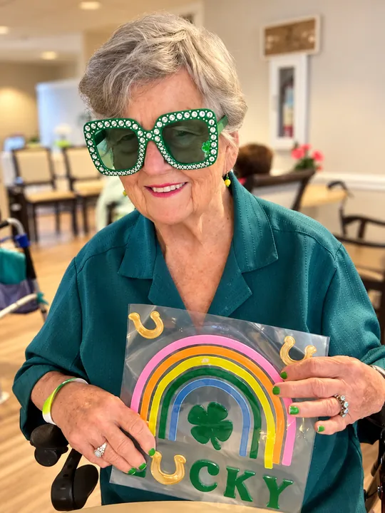 A resident in green glasses holding a rainbow and shamrock craft that reads Lucky